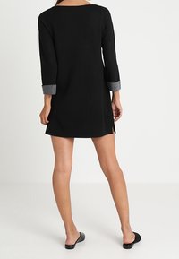 Abito in maglia nero con maniche grigie a tre quarti arrotolate, spacchi laterali e una vestibilità morbida. Tessuto liscio e scollatura arrotondata.