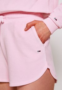 Světle růžové šortky z měkkého materiálu, s elastickým pasem na šňůrku, boční kapsou a vyšitým detailem loga na lemu.