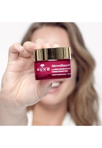 Krem NUXE Merveillance Lift w czerwonym szklanym słoiku ze złotą pokrywką. Etykieta zawiera tekst w białym i czarnym, który szczegółowo opisuje produkt.