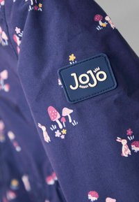 Granatowy materiał z kolorowym wzorem kwiatów i zwierząt, z grzybami i królikami. Zawiera teksturowaną niebieską metkę z logo "JoJo".