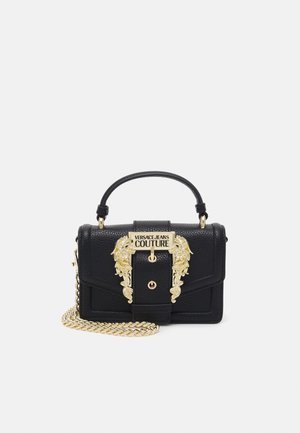 Czarna torebka Versace Jeans Couture z złotą ozdobną klamrą, górnym uchwytem i złotym łańcuszkiem na białym tle.