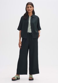 Donkergroene, gestructureerde overhemdd met korte mouwen, gecombineerd met bijpassende wijde broek en groene sandalen.