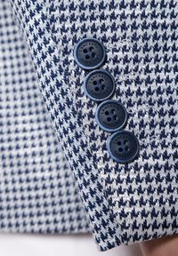 Granatowy i biały materiał w wzór houndstooth z teksturowanym splotem; posiada cztery granatowe guziki z wytłoczonym logo na mankiecie.