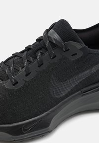 Pantofii de alergare negri prezintă un superior din tricot texturat, șireturi plate și un design elegant, cu un logo Nike vizibil și o talpă amortizată.