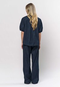 Denim outfit met een donkerblauwe top met pofmouwen en een wijde broek, beide met een gladde textuur en een strak, eenvoudig ontwerp.