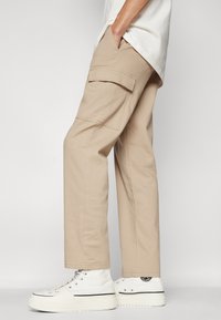 Beige cargobroek met zijzakken, rechte pasvorm en gemaakt van katoen, gecombineerd met witte hoge sneakers met een zwart logo.