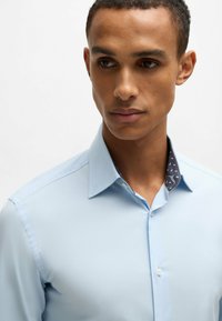 Himmelblaues Hemd mit Kragen, das eine dunkelnavyausgekleidete Innenseite mit einem weißen Muster hat. Glatte Textur, taillierte Passform.