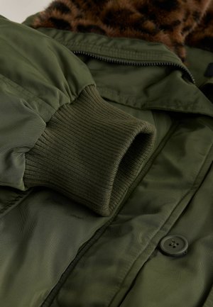 Giacca isolante verde con polsini a coste, chiusura con zip e collo in pelliccia marrone a motivo leopardato. Include un dettaglio con bottone nero.
