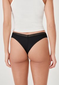 String nera a costine con pizzo, caratterizzata da un taglio alto delle gambe e una copertura minima sul retro. Il tessuto sembra morbido con una sottile texture.