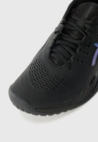 Close-up of a black ASICS sneaker with textured toe, black laces, mesh upper, and iridescent purple logo on the side.
