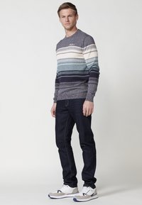 Gestreepte gebreide trui in blauw, crème en marineblauw; ronde halslijn; gecombineerd met donkere jeans en witte sneakers. Gelaagd weefsel met verschillende strookbreedtes.
