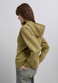 Olivgrön hoodie med mjuk textur, en huva med dragsko och ribbade muddar, tillsammans med ljusblå jeans. Enkel och avslappnad design.