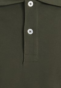 Polo vert foncé en gros plan montrant deux boutons blancs et la texture du tissu tricoté.