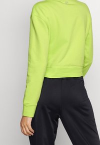 Skrócona bluza w jasnym neonowym zielonym kolorze, z okrągłym dekoltem, długimi rękawami i ściągaczami. Połączona z czarnymi spodniami, z minimalnymi detalami.