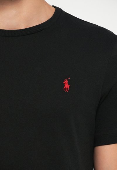T-shirt noir à manches courtes en coton, avec un col rond et un petit logo de polo rouge brodé sur la poitrine gauche.