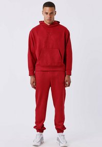 Sudadera roja con bolsillo canguro, puños elásticos y cintura elástica, combinada con pantalones jogging rojos a juego con tobillos elásticos y detalle de logo.