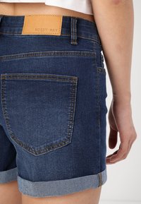 Blå denimshorts med uppvikt kant, med en läderetikett "NOISY MAY" på baksidan och sydda bakfickor.