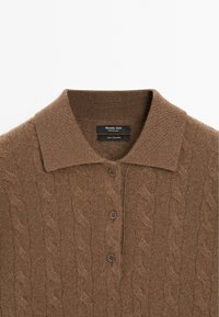 Braunes Kaschmir-Polo mit einer Kabelstricktextur, charakterisiert durch einen klassischen Kragen und drei braune Knöpfe entlang der Knopfleiste.