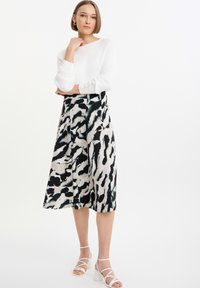 Top de manga larga blanco con ribetes y detalles de botones, combinado con una falda de estampado animal en blanco y negro de longitud media, acentuado con sandalias de tacón bloque blancas.