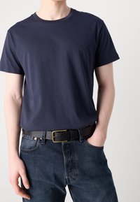 Marine crew-neck t-shirt lavet af bomuld, parret med mørke denim bukser og et sort bælte med en messingspænde, der understreger en afslappet stil.
