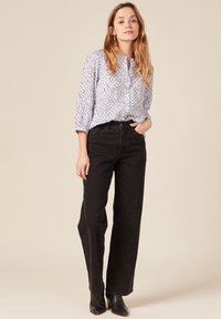 Blusa bianca a maniche lunghe con un motivo geometrico blu, abbinata a jeans neri a vita alta e stivaletti neri. Design semplice e pulito.