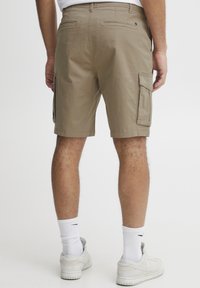 Beige cargo rövidnadrág, több oldalsó zsebbel, laza szabású, térd fölött végződő szegéllyel. Fehér zoknival és sportcipővel párosítva.
