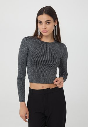 Top corto a maniche lunghe nero e argento con scollatura tonda, caratterizzato da un design aderente e tessuto texture. Abbinato a pantaloni neri a vita alta.