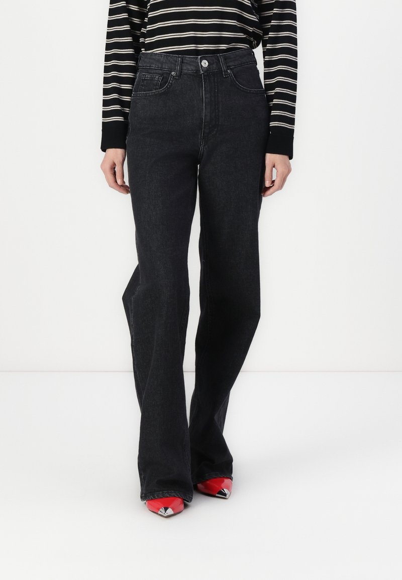 Svarta utsvängda jeans med hög midja, tillverkade av denim, med framfickor och subtila sömdetaljer. Matchas med röda spetsiga klackar.