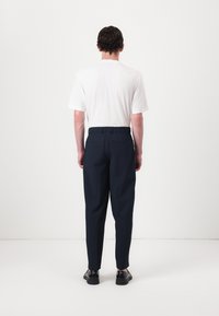 Pantalons bleu marine avec une coupe décontractée, une taille élastique et un design minimaliste. Portés avec un t-shirt blanc uni et des chaussures noires.