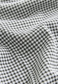 Tela de patrón de pata de gallo en blanco y negro con una superficie texturizada, que presenta pequeñas formas dentadas que se repiten, dispuestas en suaves pliegues.