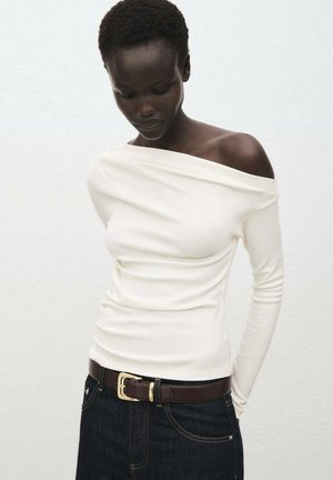 Witte, off-shoulder top met lange mouwen en een aansluitend design, gecombineerd met donker denim jeans en een bruine riem met een gouden gesp.