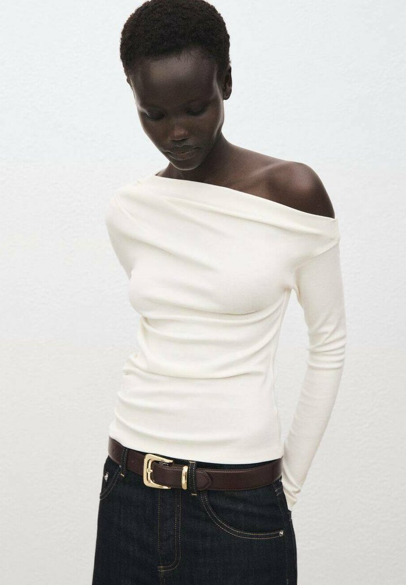 Witte, off-shoulder top met lange mouwen en een aansluitend design, gecombineerd met donker denim jeans en een bruine riem met een gouden gesp.