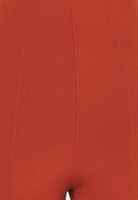 Gros plan sur un tissu orange à nervures serrées avec des coutures verticales, mettant en valeur la texture et les détails de couture sur des vêtements.