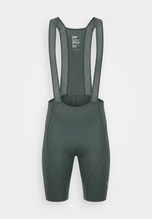 Tamnozelene biciklističke bretelice s podstavljenim sjedalom i širokima elastičnim naramenicama na bijeloj pozadini.