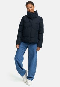 Marinblå puffjacka med hög krage, diamantquiltad mönster och framförande knappdetaljer. Bärs med vida blå jeans och vita sneakers.