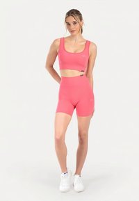 Strakzittende roze sportbeha en bijpassende shorts met hoge taille van rekbare stof. Heeft een gladde textuur en subtiele logo-accenten.