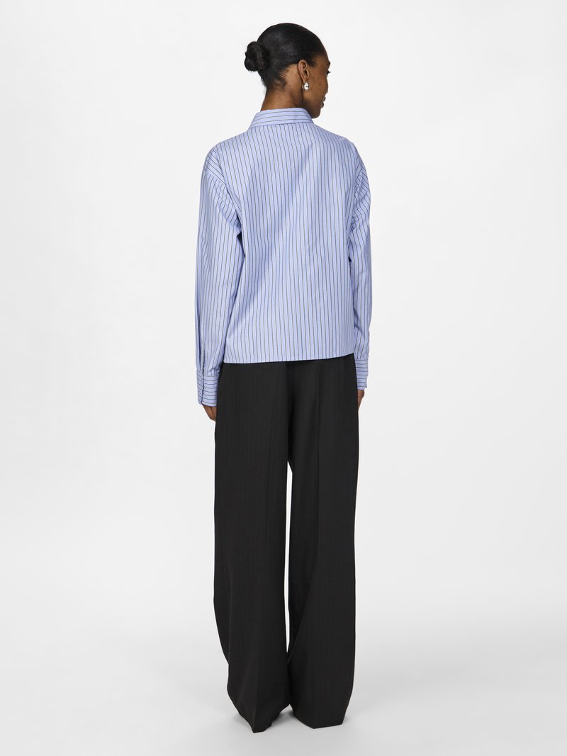 Blauw-wit gestreept shirt met een kraag, lange mouwen en een relaxte pasvorm, gecombineerd met hoge zwarte wijde broekspijpen.