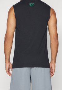 Chemise noire sans manches avec une texture lisse, présentant un petit logo vert brodé à l'arrière du col. Accompagnée d'un short gris.