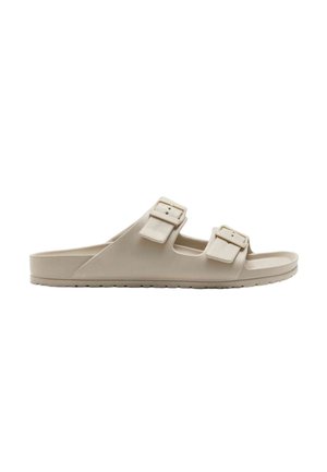 Beige Hausschuh-Sandale mit zwei verstellbaren Schnallenriemen und strukturierter Sohle, entworfen für den Freizeitgebrauch und Komfort.