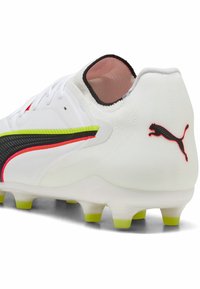 Valkoinen jalkapallokengän piikkari, jossa musta, neonkeltainen ja punainen Puma-logo, vihreät nastat ja matala nilkkakärki.