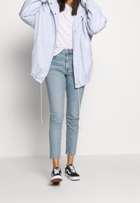 Giacca oversized bleu chiaro con cordino, abbinata a jeans in denim chiaro a vita alta e sneakers nere Vans. Outfit casual.