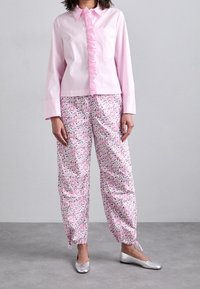 Pink cotton shirt with ruffle detail and pocket, paired with lightweight floral pajama pants featuring a drawstring hem. Silver ballet flats.