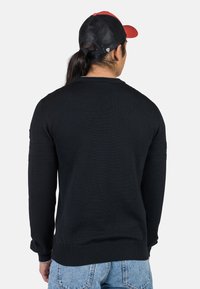 Schwarzer Strickpullover mit langen Ärmeln, gerippten Bündchen und Saum, der über strukturierte Details an den Schultern und einen lässigen Schnitt verfügt.
