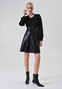 Zwarte jurk met opgeblazen mouwen, een aansluitend lijfje en een uitlopende rok. Draag met glanzende zwarte enkellaarsjes met zilveren studs en spitse neuzen.