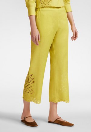 Gele linnen cropped broeken met geborduurde uitsnijdingen aan de zoom, met golvende randen. Gepaard met bruine platte schoenen.