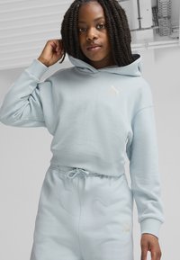 Helles blaues Hoodie mit Kordelzug, das ein PUMA-Logo trägt. Der Stoff wirkt weich und die Bündchen sind gerippt. Kombiniert mit passenden Jogginghosen.