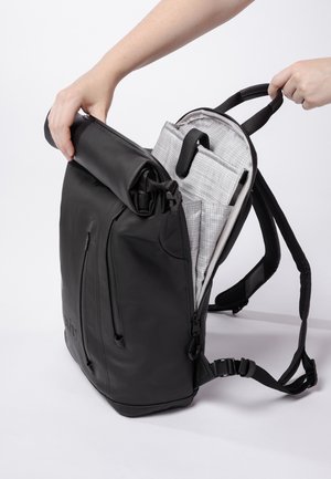 Schwarzer Rolltop-Rucksack mit einer strukturierten Oberfläche, mehreren äußeren Reißverschlüssen und einem hellgrauen Innenraum mit organisierten Taschen.