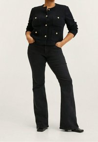 Marineblå tekstureret jakke med guldknapper, to frontlommer, parret med sorte flared jeans og sorte ankelstøvler. Simple, skræddersyet design.