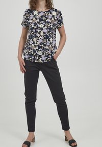 Blommig kortärmad topp i mörk marinfärg och pastellfärger, i kombination med tighta svarta byxor och svarta sandaletter. Slät tygkvalitet med en avslappnad passform.