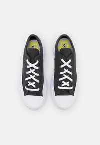 Svarta canvas-sneakers med vita gummisulor, med vita snörningar och en stjärnlogotyp på innersulan. Ytan är slät och flexibel.